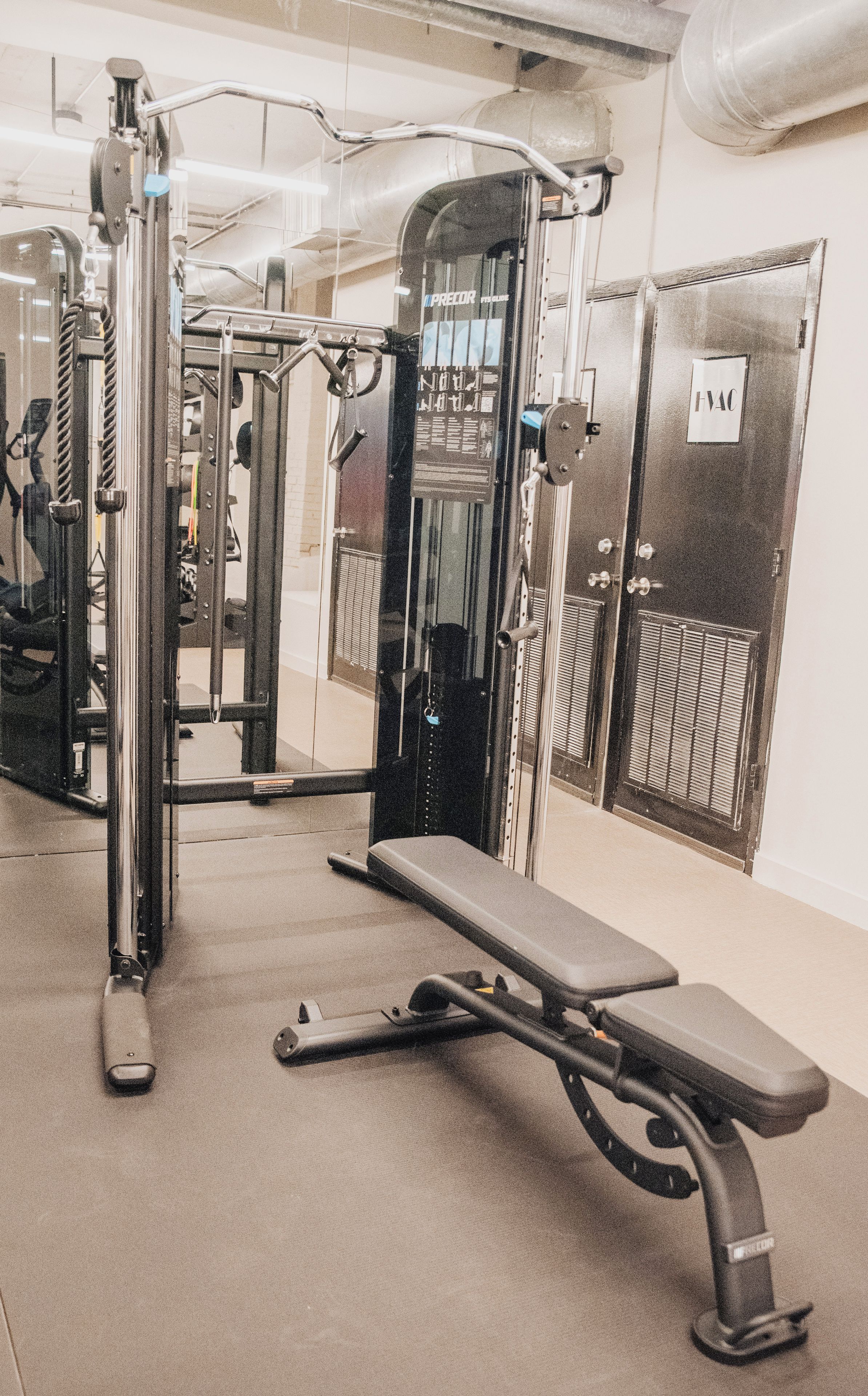 A gym with exercise equipment, a bench, and a door labeled 'HVAC'.