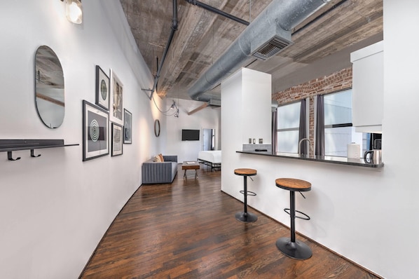 A modern interior with a wooden floor, white walls, and a kitchen area with a window. - Reside Houston Downtown A Wyndham Residence (Houston)