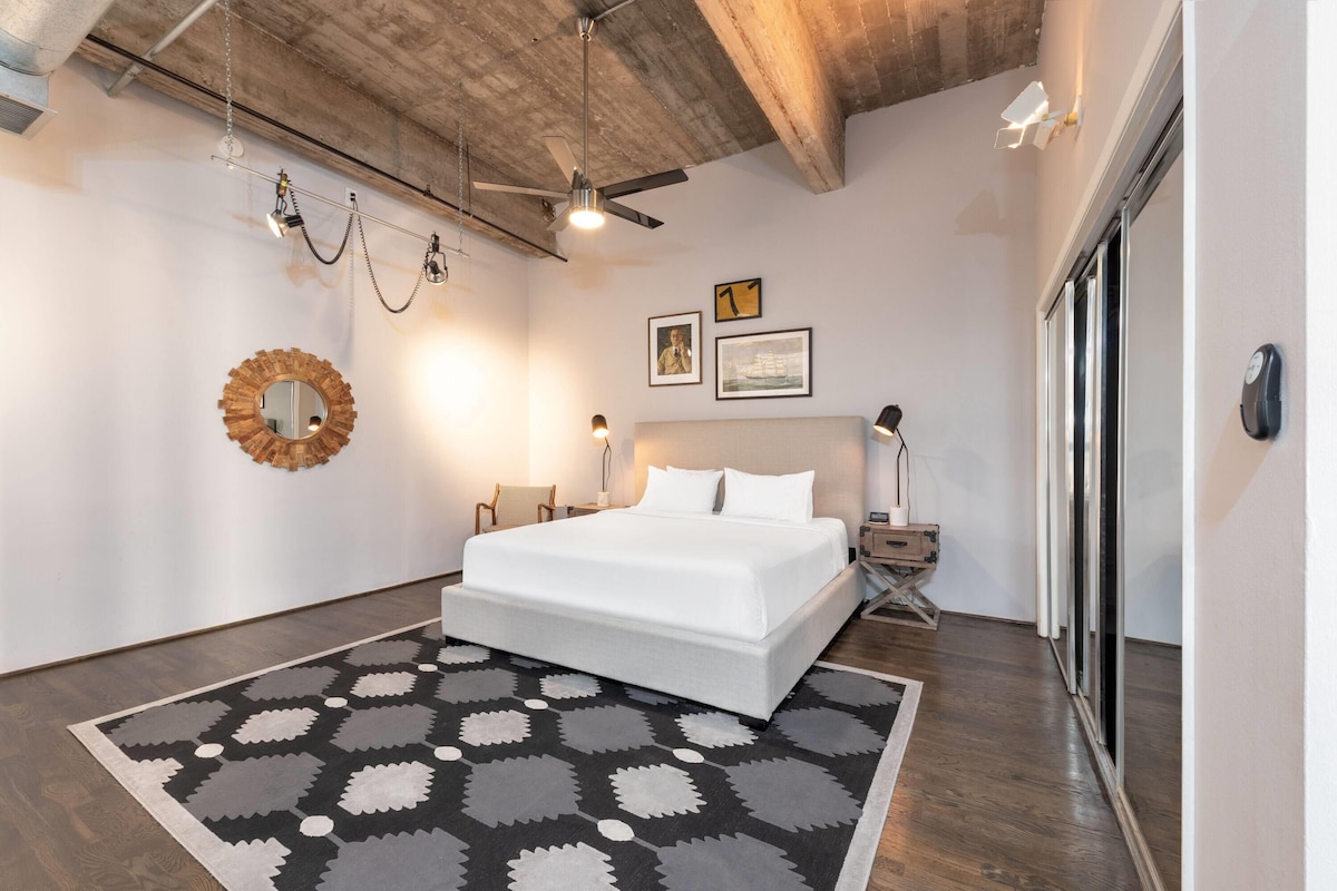 Un dormitorio con cama, espejo redondo, ventilador de techo y alfombra estampada.
