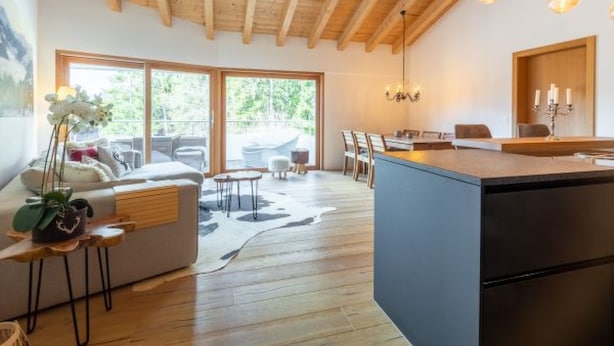 Eine moderne Küche mit Holzbalken, ein Essbereich mit Tisch und Stühlen sowie ein großes Fenster mit Blick ins Grüne.