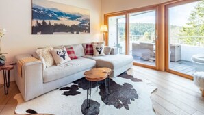 Ein modernes Wohnzimmer mit einem weißen Sofa, einem Holztisch, einem Kuhfellteppich und einem Gemälde einer Berglandschaft an der Wand.