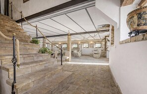 Eine Steintreppe führt zu einem geräumigen Zimmer mit hoher Decke, großen Fenstern und einem Kamin.