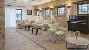 Een kamer met een piano, banken met bloemenprint, een salontafel en een open haard.
