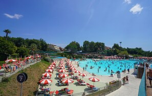 Uma grande piscina ao ar livre rodeada por guarda-sóis vermelhos e brancos, com um céu azul límpido acima.