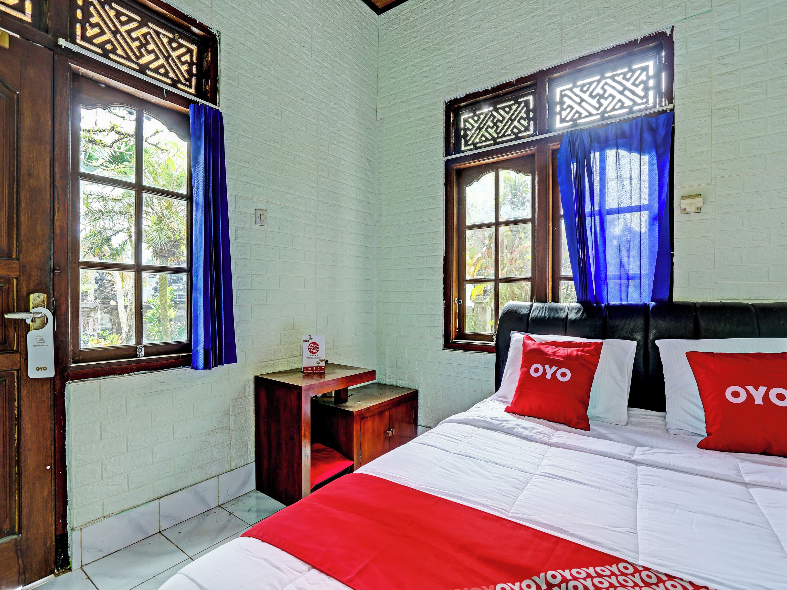 A room with a bed, a nightstand, a window with curtains, and a door with a handle.