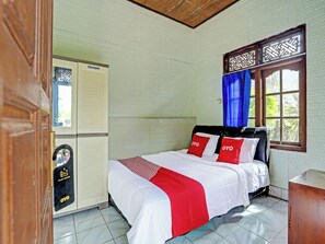 A hotel room with a bed, a wardrobe, a window with curtains, and a tiled floor.