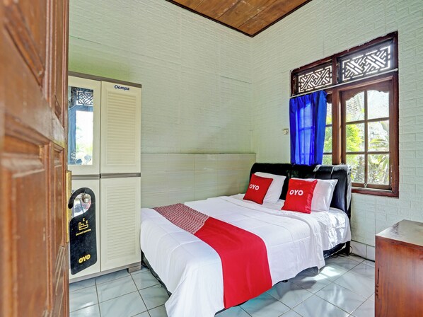 A hotel room with a bed, a wardrobe, a window with curtains, and a tiled floor.