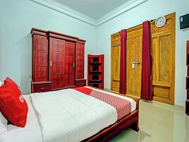 Quarto com cama, roupa de cama vermelha e branca, um travesseiro vermelho, armários de madeira, uma cortina vermelha e um relógio de parede.