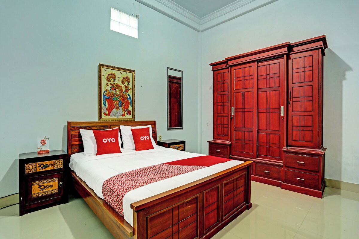 A bedroom with a wooden bed, red pillows, a nightstand, a wardrobe, and a painting on the wall.