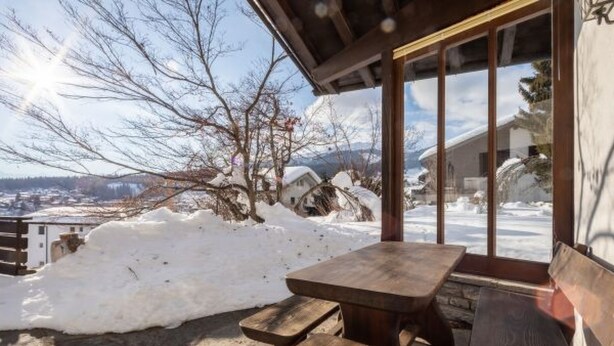 Un banco y una mesa de madera frente a un edificio, con vista a un paisaje nevado y árboles.