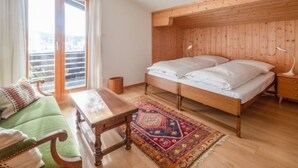 Un dormitorio con cabecera de madera, cama con ropa de cama blanca, sofá verde, mesita de noche de madera y alfombra estampada.