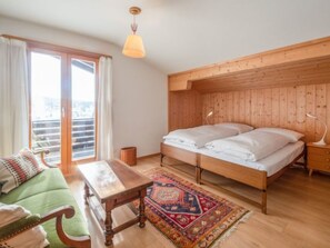 A bedroom with a wooden headboard, a bed with white linens, a green sofa, a wooden nightstand, and a patterned rug. - Casa Murissen by Interhome (Flims)