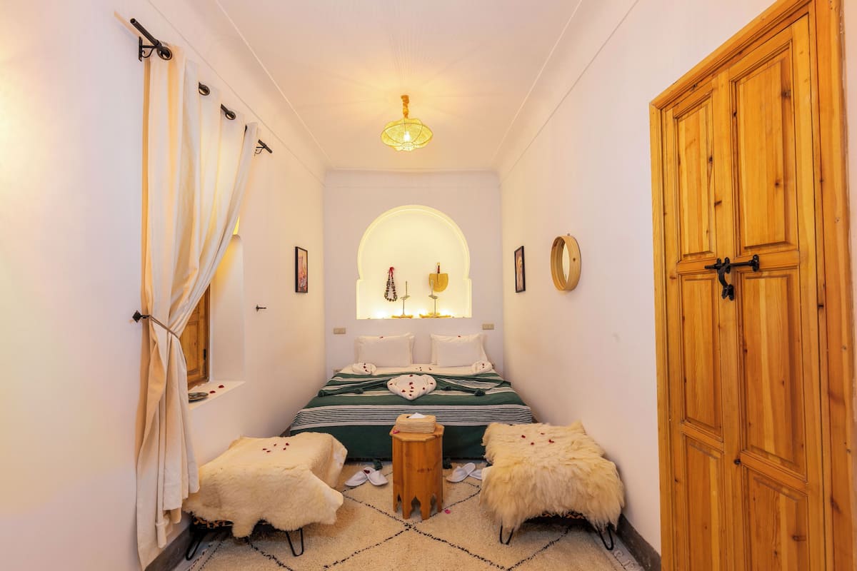 A narrow hallway leading to a bedroom with a bed, a wooden wardrobe, and a small stool.