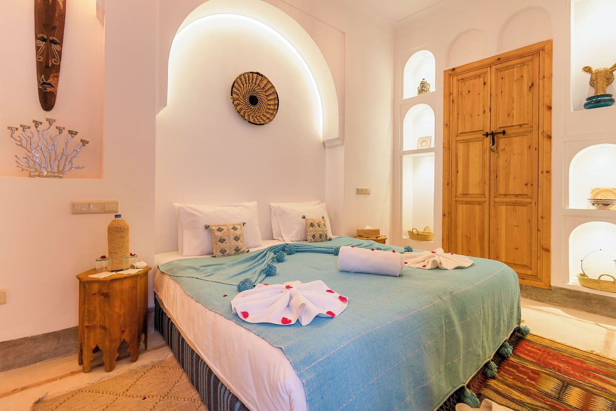 A bedroom with a bed, wooden wardrobe, and decorative wall art.