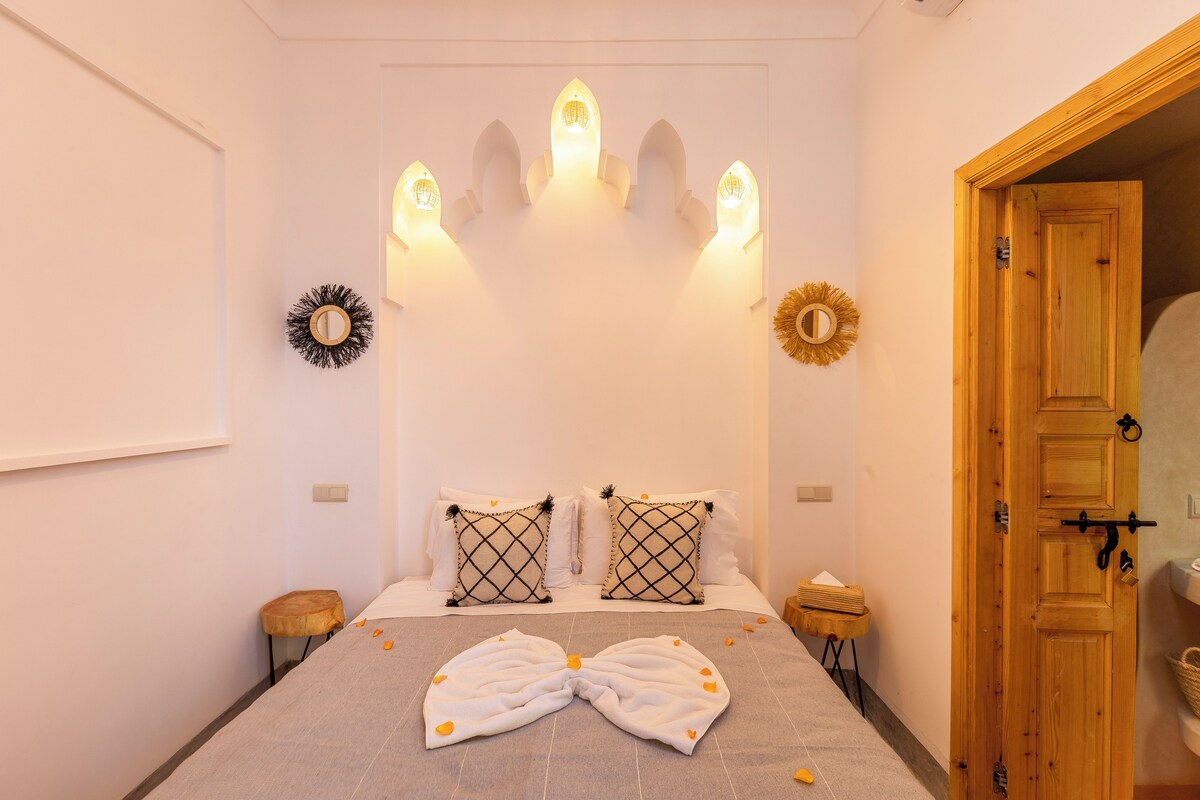 A bedroom with a bed, two bedside tables, a wooden door, and wall sconces.