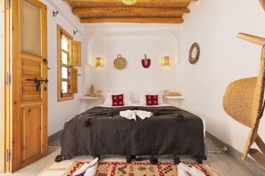A bedroom with a bed, wooden door, wall-mounted lights, and a woven chair. - Riad Mama Square (Marrakech)