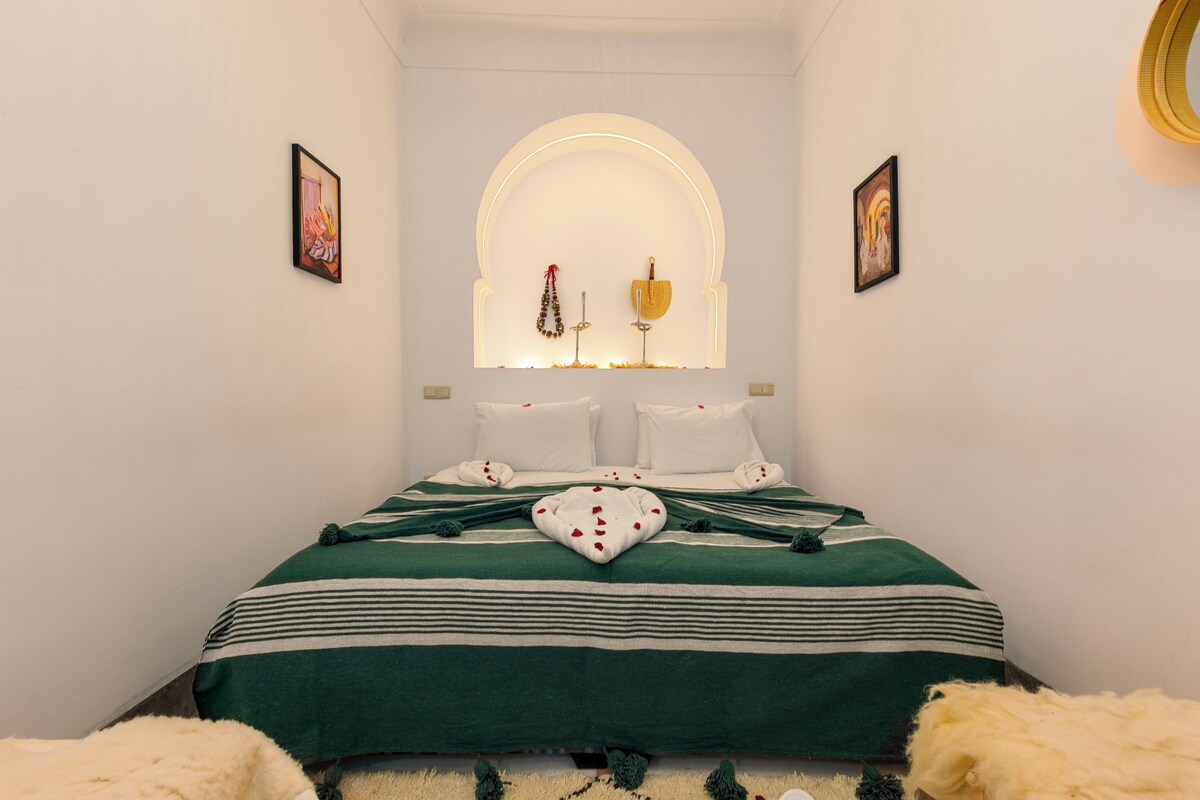 A neatly arranged bedroom with a bed, pillows, a heart-shaped decoration, and a window with a decorative arch.