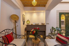 A cozy room with a wooden ceiling, a dining table with a vase of flowers, and a sofa with a striped pillow. - Riad Mama Square (Marrakech)