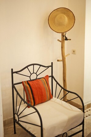 A metal chair with a cushion and a woven hat stand against a wall. - Riad Mama Square (Marrakech)