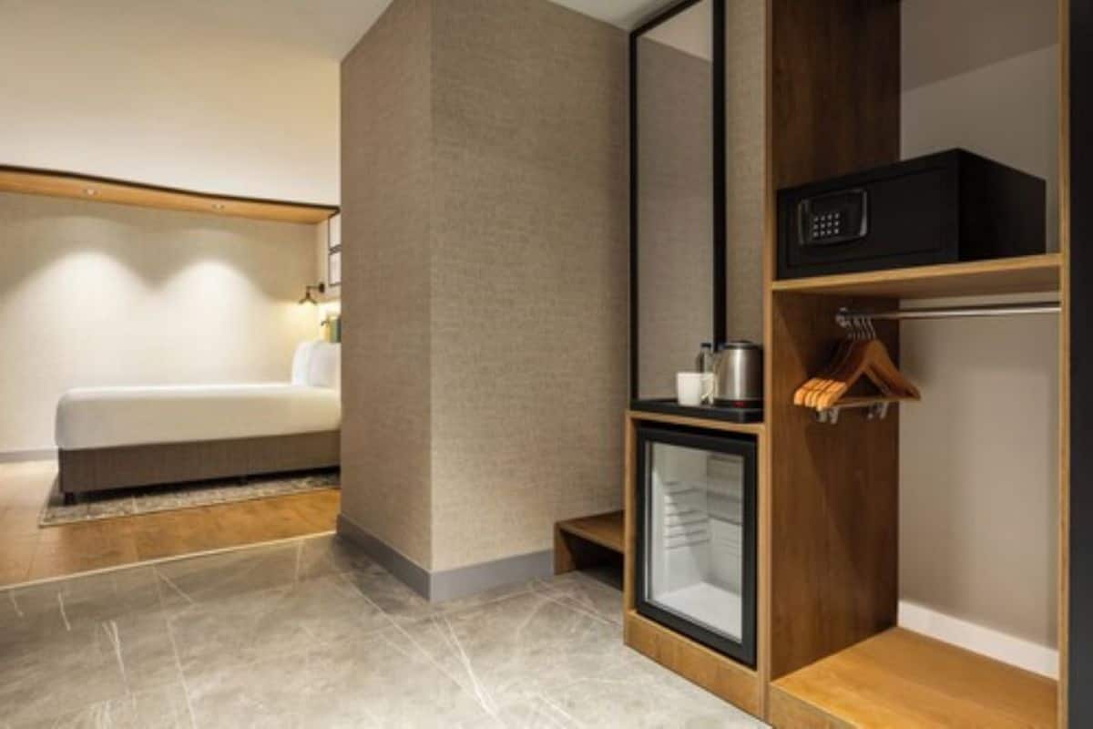 Ein modernes Hotelzimmer mit einem Bett, einer kleinen Schranke mit einer Mikrowelle und einem hölzernen Regal mit einem Kleiderhaken.