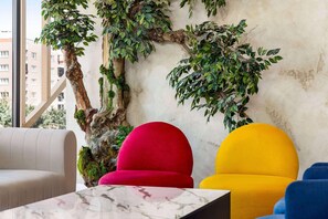 Una habitación con un gran tronco de árbol, una silla roja, una silla amarilla y una silla azul.