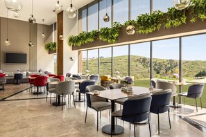 A modern dining area with large windows, a flat-screen TV, and a variety of seating arrangements. - Ramada Encore by Wyndham Istanbul Arnavutkoy (Istanbul)