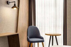 Ein modernes Zimmer mit einem dunkelblauen Polsterstuhl, einem runden Holztisch und einer Wandleuchte.