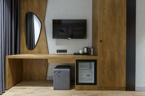 Una habitación moderna con un escritorio de madera, televisión montada en la pared, un refrigerador pequeño y un banco.
