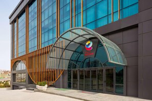 Un edificio moderno con grandes ventanales, una entrada de vidrio curvo y un logotipo con un diseño colorido.