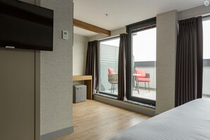 A hotel room with a bed, a TV, a small desk, a chair, and a balcony with a view. - Ramada Encore by Wyndham Istanbul Arnavutkoy (Istanbul)