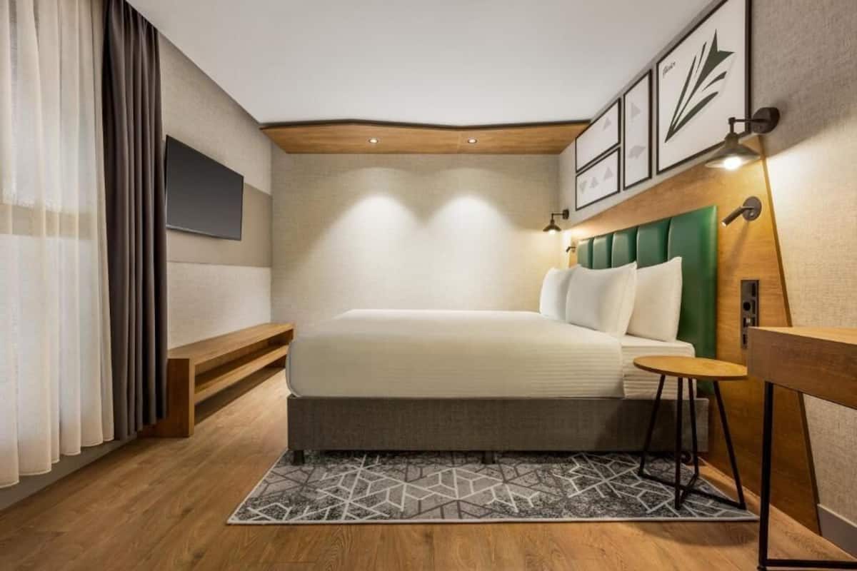 Ein modernes Hotelzimmer mit Bett, kleinem Tisch, Fernseher und einem grünem Kopfteil.