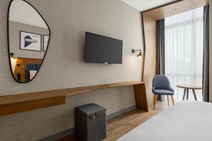 A hotel room with a large bed, a flat-screen TV mounted on the wall, a small stool, a chair, and a window with curtains. - Ramada Encore by Wyndham Istanbul Arnavutkoy (Istanbul)
