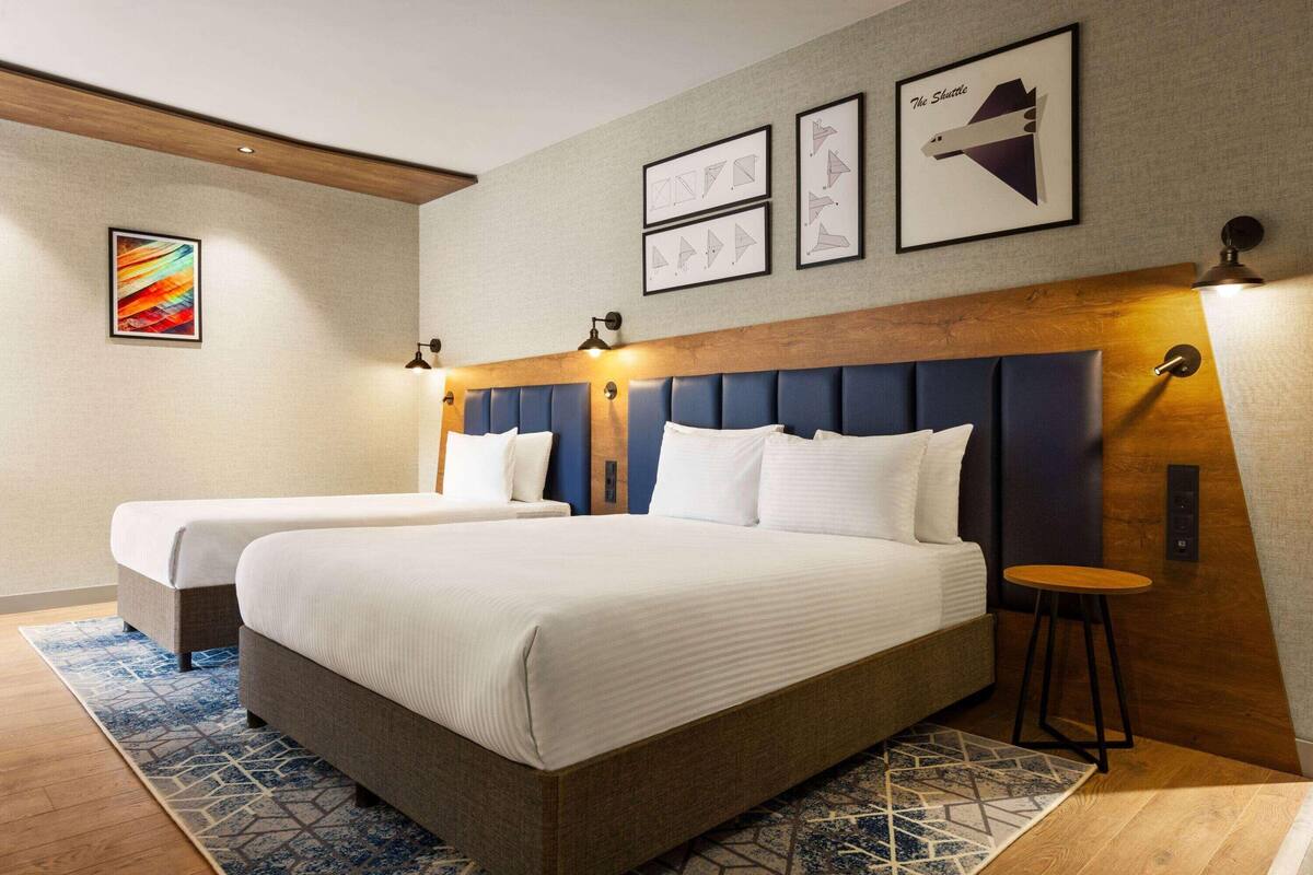 Ein Hotelzimmer mit zwei Betten, einem hölzernen Kopfteil, einem kleinen Hocker und Bildern an den Wänden.