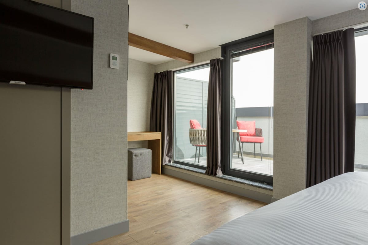 Habitación de hotel con cama, televisor, escritorio pequeño, silla y balcón con vistas.