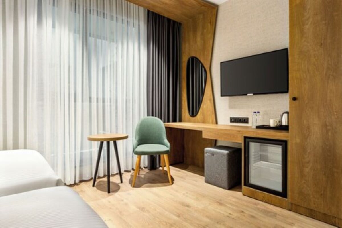 Habitación de hotel con cama, escritorio con silla, televisor, mini refrigerador y cafetera.