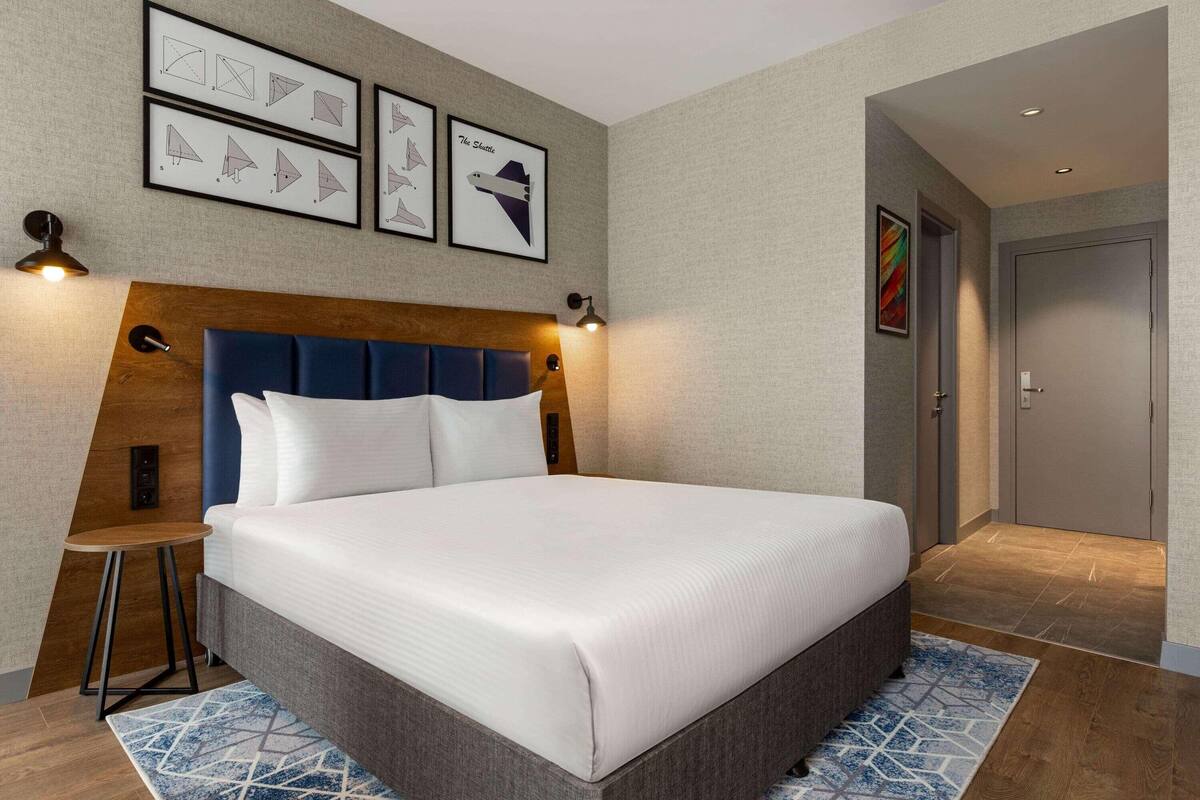 Ein Hotelzimmer mit einem großen Bett, einem Holzkopfteil, einem kleinen Nachttisch und gerahmten Kunstwerken an der Wand.