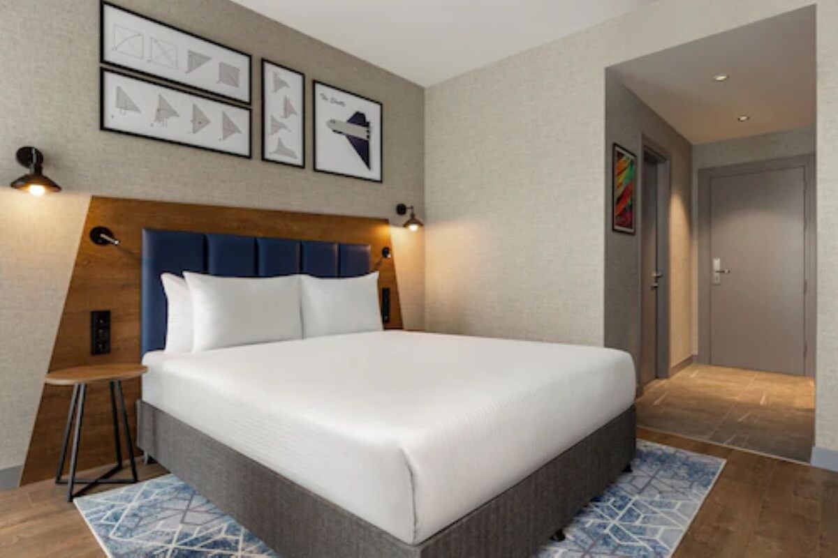 Habitación de hotel con una cama grande, un cabecero de madera, un escritorio con una silla y cuadros en la pared.