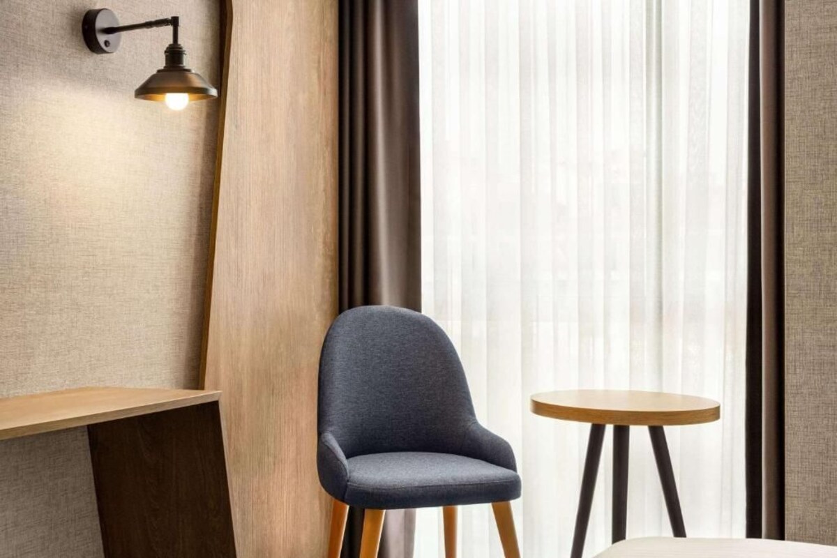 Una habitación con una sola silla, una mesita redonda pequeña, una lámpara de pared y cortinas traslúcidas.