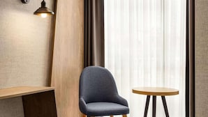 Una habitación con una sola silla, una mesita redonda pequeña, una lámpara de pared y cortinas traslúcidas.