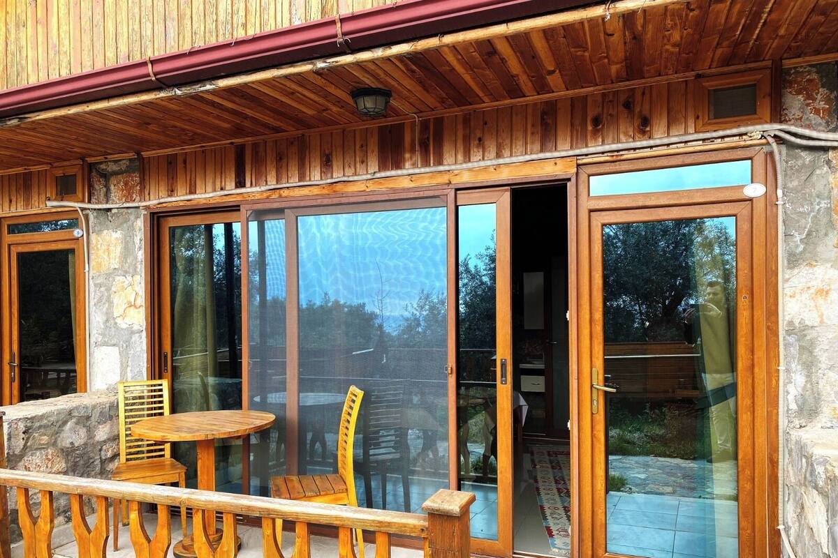 Un balcon en bois avec une table et des chaises, de grandes portes-fenêtres coulissantes et un mur en pierre.