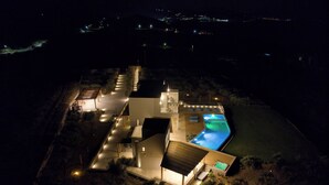 A modern house with a swimming pool, a covered patio, and a well-lit driveway. - Villa Paradiso Mochlos (Sitia)
