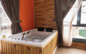 Una bañera de madera con dos grifos, una pared de madera y una ventana con cortinas.