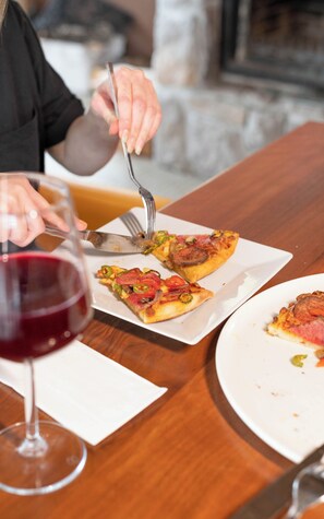 Et spisebord med pizza, et glas rødvin og en gaffel.