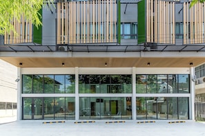 A modern building with a glass facade, a covered entrance, and a balcony with vertical slats. - Infinite Hotel @kaset-senanikom (Bangkok)