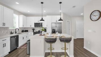 A modern kitchen with white cabinetry, stainless steel appliances, a central island, and two bar stools.