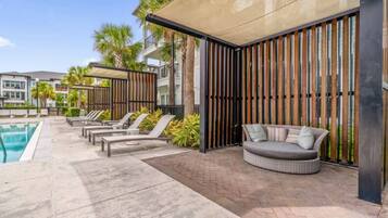 A poolside area with lounge chairs, a sofa, and a covered seating area with vertical wooden slats.
