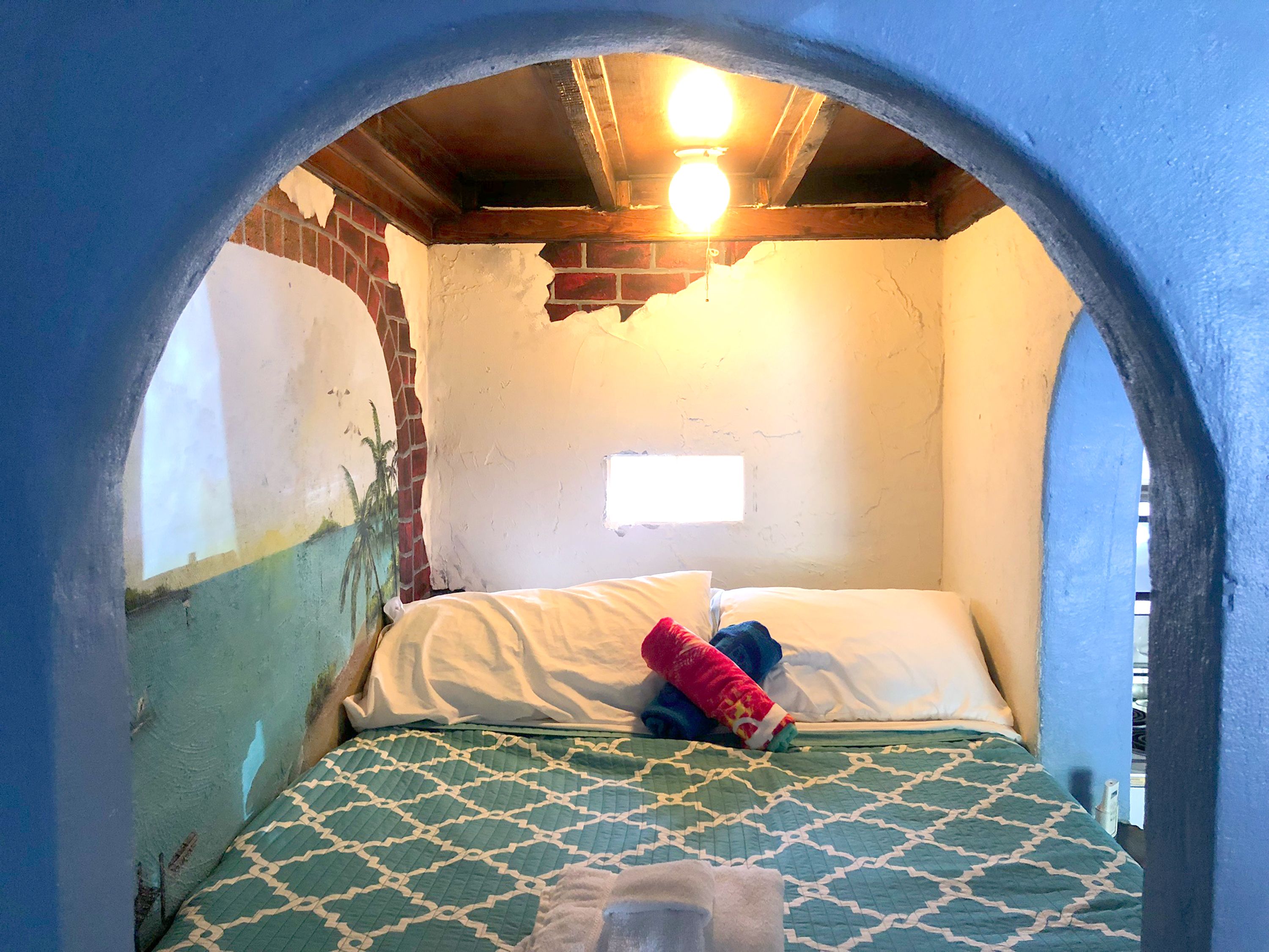 A room with a bed, a window, and a wall with peeling paint.