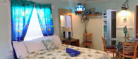 Un dormitorio con cama, una silla, una mesa y una lámpara colgante.