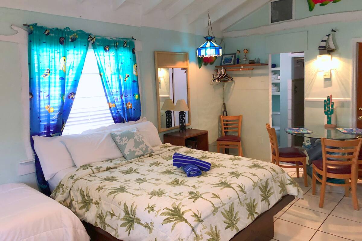 Un dormitorio con cama, una silla, una mesa y una lámpara colgante.