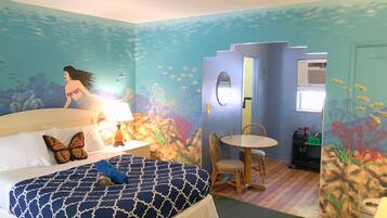 A room with a bed, a table, and chairs, decorated with an underwater theme including a mural of a mermaid and fish.